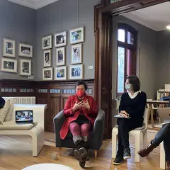 Quatre personnes masquées discutent dans un salon orné de cadres. Une femme en rouge est au centre, semblant raconter une histoire lors d'une résidence d'écriture.