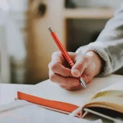 Main d'une personne écrivant avec un stylo rouge dans un carnet, un sujet d'écriture spontanée.