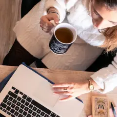 Une femme boit une tasse de thé en travaillant sur son ordinateur portable, prête à déposer un manuscrit.