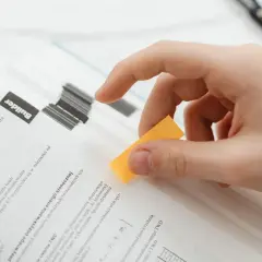Main d'une personne tenant un marque-page jaune sur un livre ouvert, comme une figure de style pour marquer une page importante.