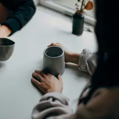 Deux personnes partagent un moment autour de tasses. Leurs mains se frôlent, comme dans une succession de répliques courtes, un dialogue silencieux.
