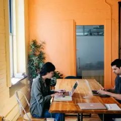 Deux personnes travaillent sur leurs ordinateurs portables dans un bureau lumineux aux murs orange. Ils apprennent à protéger ses œuvres gratuitement.