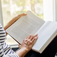 Une personne lit un livre près d'une fenêtre. Les pages sont blanches, suggérant le fin du livre.