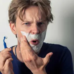 Un homme se rase, la mousse envahit sa bouche comme une figure de style pour exagérer son expression de surprise.