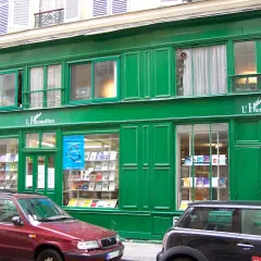 Façade verte d'une librairie L'Harmattan, vitrines remplies de livres. Une voiture rouge et une noire stationnent devant.