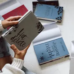Une personne feuillette des livres aux couvertures élégantes, dont "Hit delete" et "Shining snow night". Ces éditions font partie des plus belles éditions de livres.