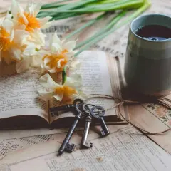 Un livre ouvert, des jonquilles, des clés anciennes et une tasse de thé. Le copyright livre est présent sur les pages jaunies.