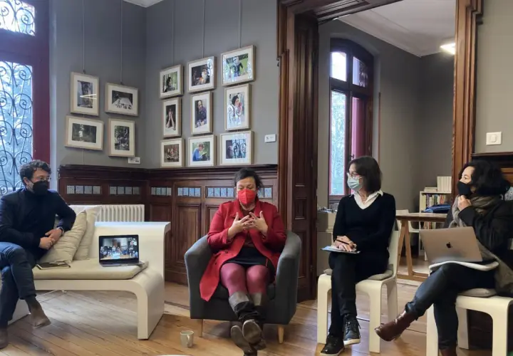Quatre personnes masquées discutent dans un salon orné de cadres. Une femme en rouge est au centre, semblant raconter une histoire lors d'une résidence d'écriture.
