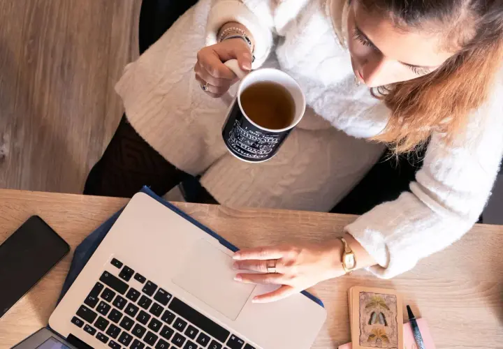 Une femme boit une tasse de thé en travaillant sur son ordinateur portable, prête à déposer un manuscrit.