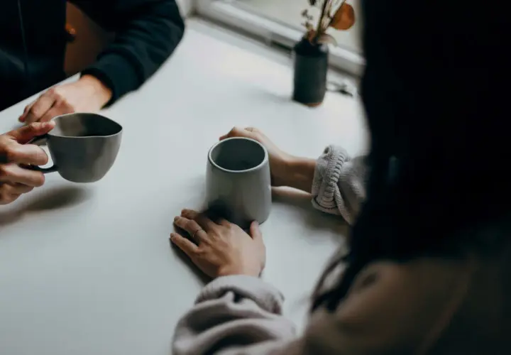 Deux personnes partagent un moment autour de tasses. Leurs mains se frôlent, comme dans une succession de répliques courtes, un dialogue silencieux.