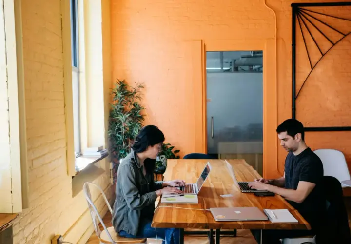 Deux personnes travaillent sur leurs ordinateurs portables dans un bureau lumineux aux murs orange. Ils apprennent à protéger ses œuvres gratuitement.