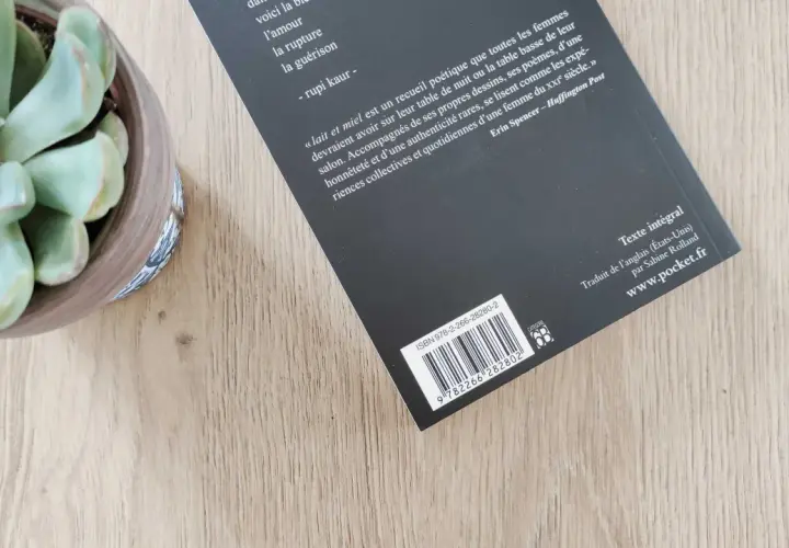 Un ean livre de poésie, "Lait et miel", est posé sur une table en bois, à côté d'une plante succulente.