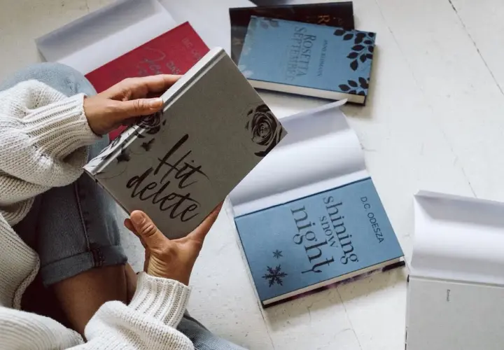 Une personne tient une jaquette de livre "Hit delete". D'autres livres sont disposés autour.