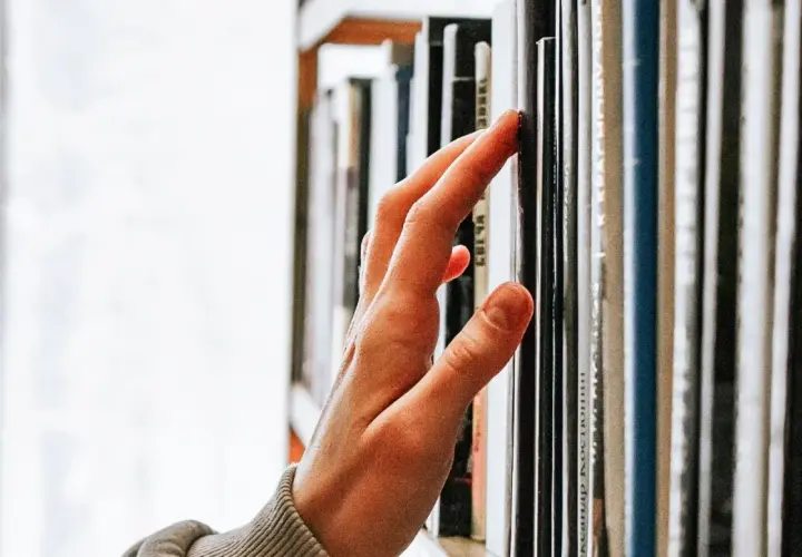 Main d'une personne effleurant une étagère remplie de livres, un voyage au cœur de la classique littérature.