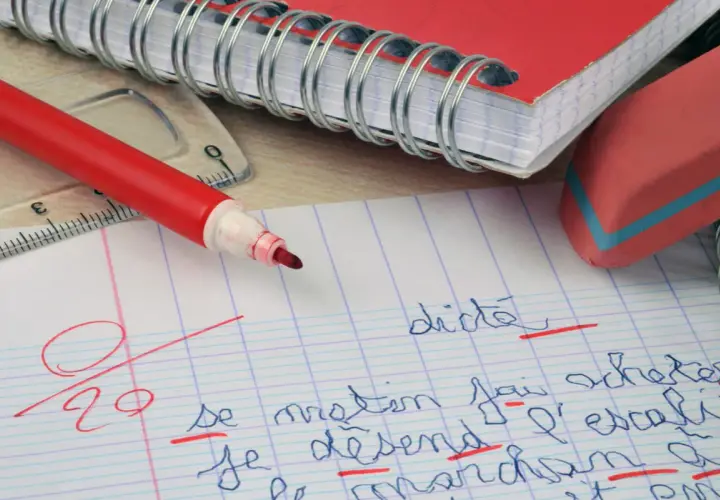 Un cahier, un stylo rouge et une gomme. La correction d'une dictée, une amplification de la figure de style "l'erreur", est en cours.