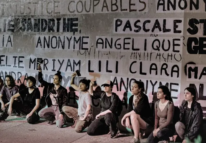 Des femmes s'agenouillent devant un mur couvert de noms, dont "Anonyme", peut-être en soutien à une écrivaine anonyme.