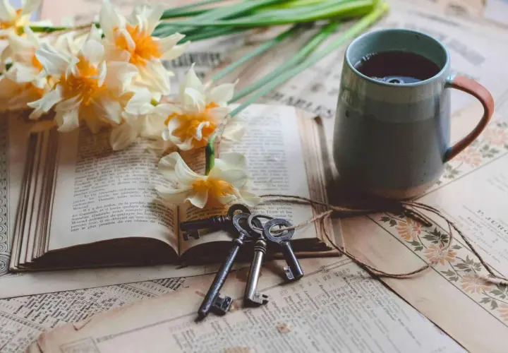 Un livre ouvert, des jonquilles, des clés anciennes et une tasse de thé. Le copyright livre est présent sur les pages jaunies.