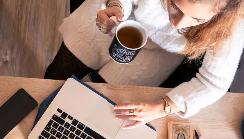 Une femme boit une tasse de thé en travaillant sur son ordinateur portable, prête à déposer un manuscrit.