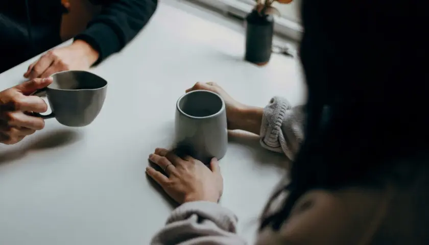 Deux personnes partagent un moment autour de tasses. Leurs mains se frôlent, comme dans une succession de répliques courtes, un dialogue silencieux.