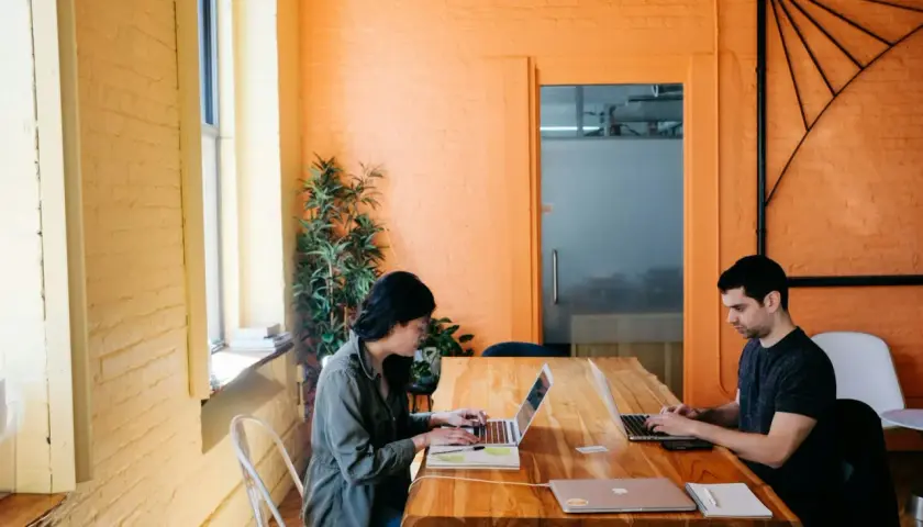 Deux personnes travaillent sur leurs ordinateurs portables dans un bureau lumineux aux murs orange. Ils apprennent à protéger ses œuvres gratuitement.