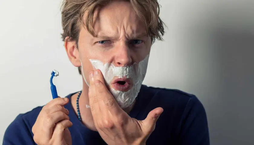 Un homme se rase, la mousse envahit sa bouche comme une figure de style pour exagérer son expression de surprise.