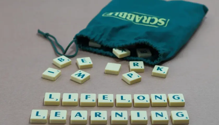 Des tuiles Scrabble forment les mots "LIFELONG LEARNING", illustrant un exemple de langage soutenu.