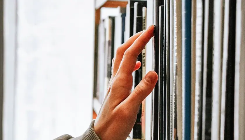 Main d'une personne effleurant une étagère remplie de livres, un voyage au cœur de la classique littérature.