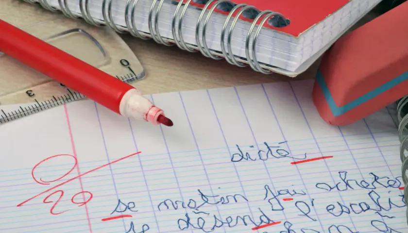 Un cahier, un stylo rouge et une gomme. La correction d'une dictée, une amplification de la figure de style "l'erreur", est en cours.
