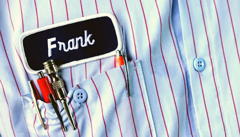 Chemise à rayures bleues et rouges avec un badge "Frank" et des stylos dans la poche. Le titre du roman est le nom du personnage principal.