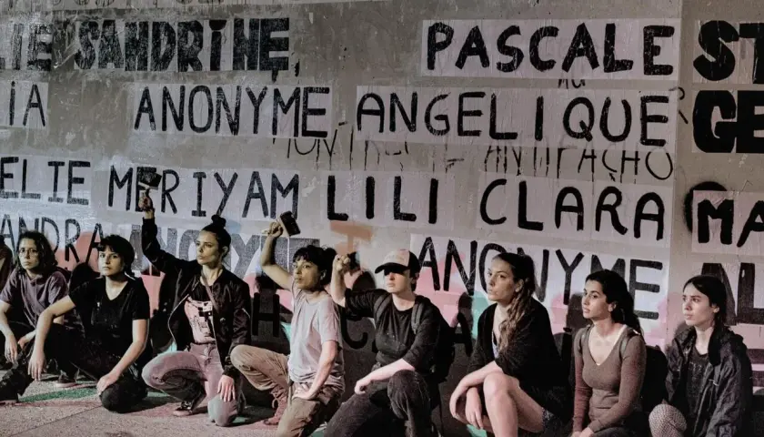 Des femmes s'agenouillent devant un mur couvert de noms, dont "Anonyme", peut-être en soutien à une écrivaine anonyme.