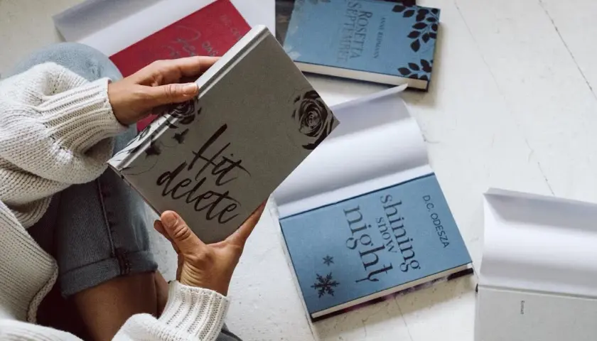 Une personne feuillette des livres aux couvertures élégantes, dont "Hit delete" et "Shining snow night". Ces éditions font partie des plus belles éditions de livres.