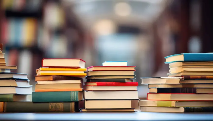 Des piles de livres colorés, formant une chaîne du livre, sur un fond flou de bibliothèque.