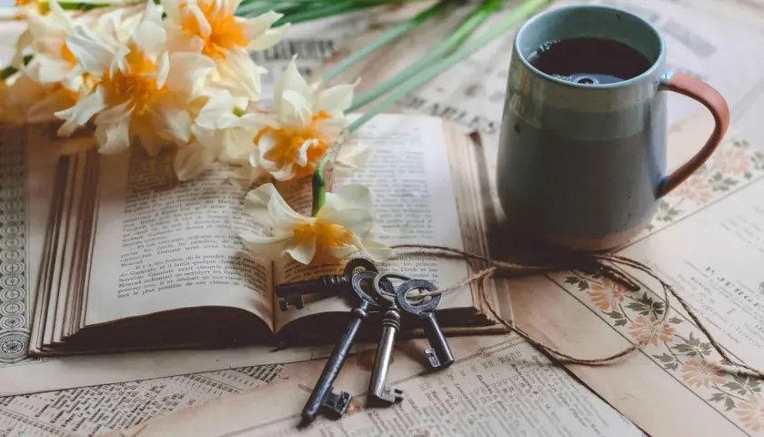 Un livre ouvert, des jonquilles, des clés anciennes et une tasse de thé. Le copyright livre est présent sur les pages jaunies.