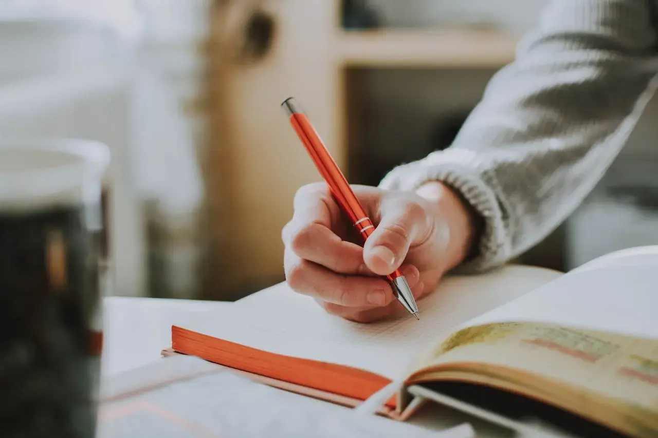 Main d'une personne écrivant avec un stylo rouge dans un carnet, un sujet d'écriture spontanée.