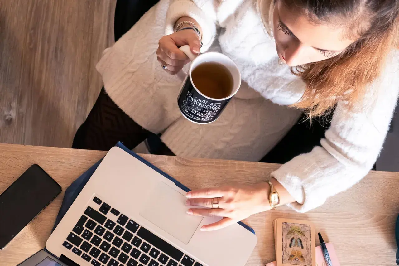 Une femme boit une tasse de thé en travaillant sur son ordinateur portable, prête à déposer un manuscrit.