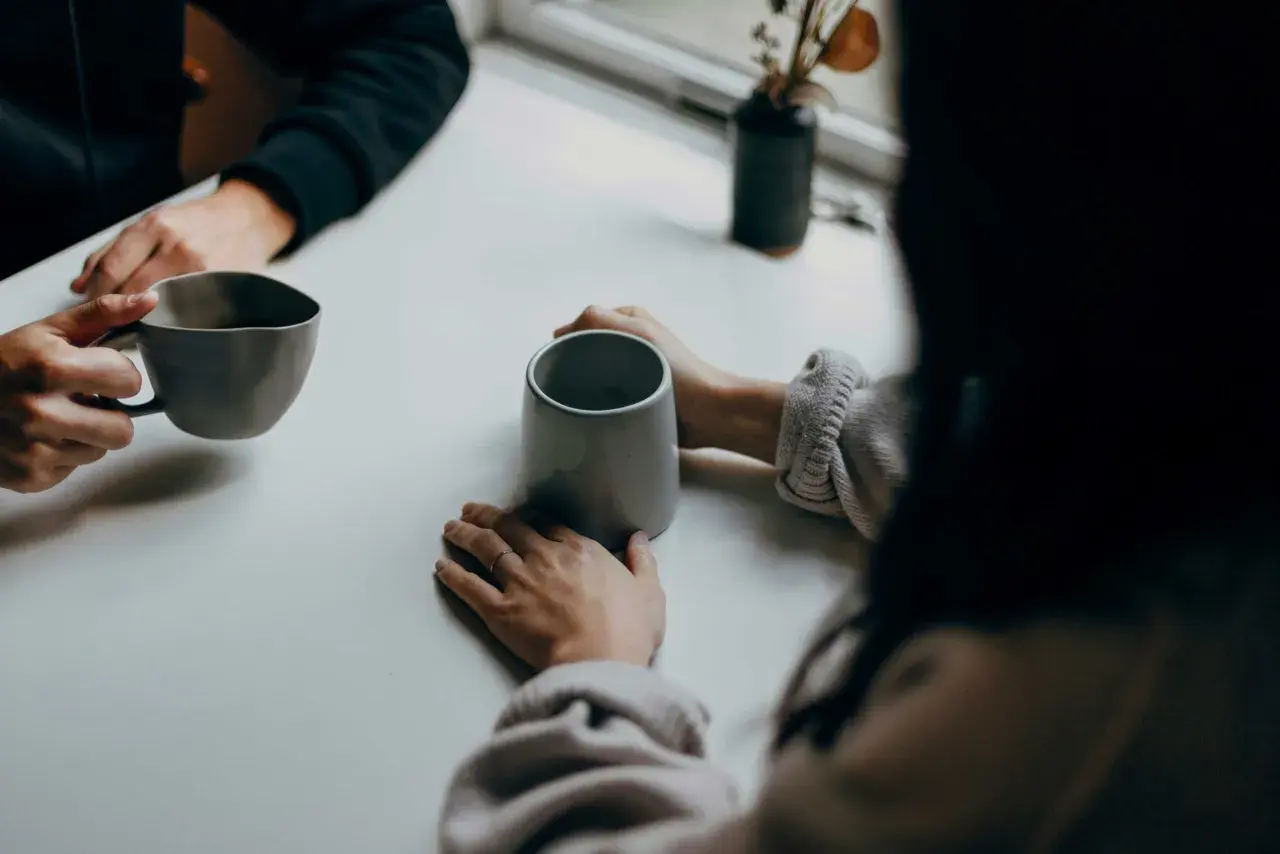 Deux personnes partagent un moment autour de tasses. Leurs mains se frôlent, comme dans une succession de répliques courtes, un dialogue silencieux.