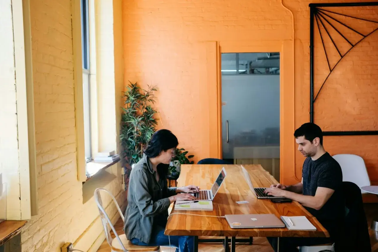 Deux personnes travaillent sur leurs ordinateurs portables dans un bureau lumineux aux murs orange. Ils apprennent à protéger ses œuvres gratuitement.