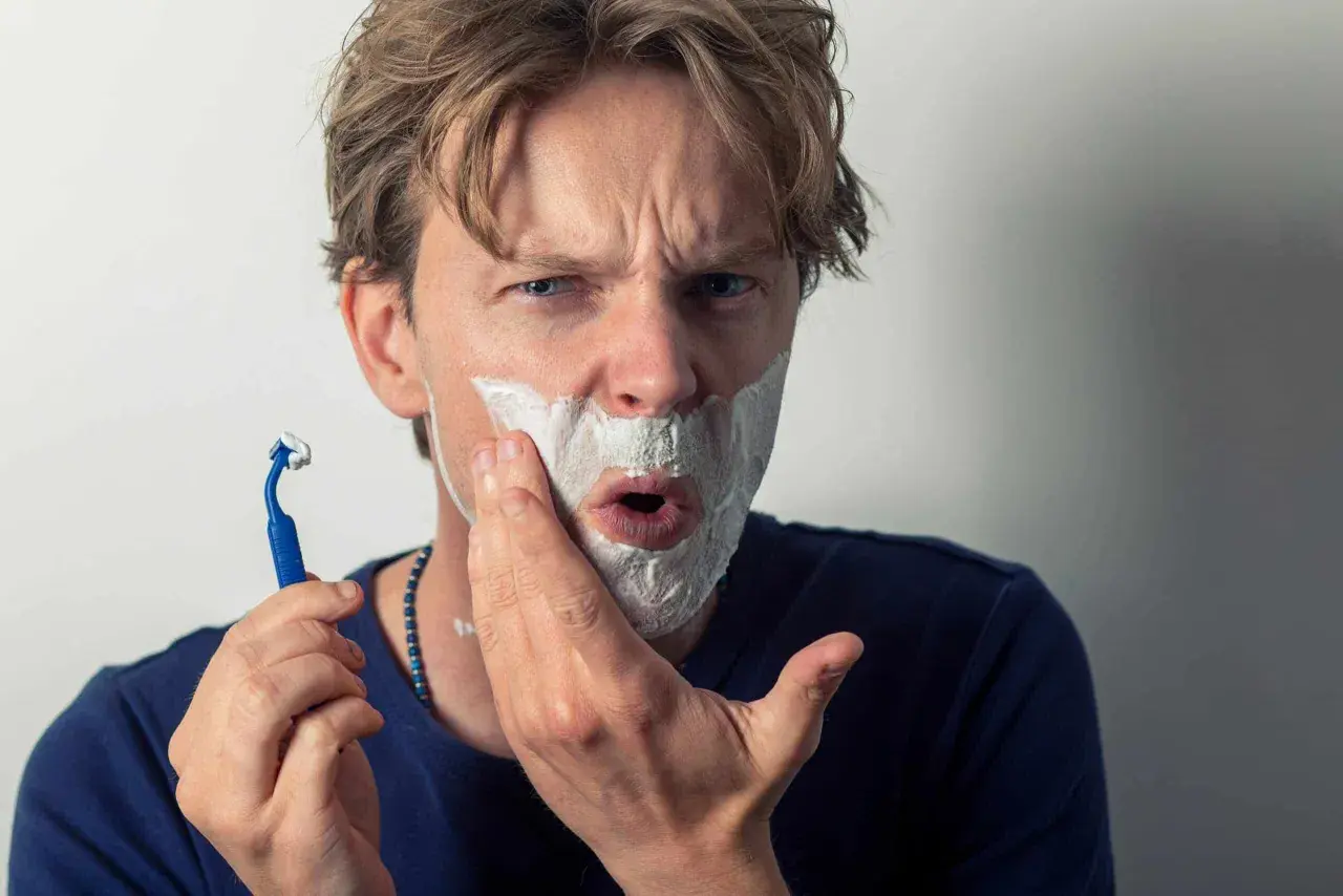 Un homme se rase, la mousse envahit sa bouche comme une figure de style pour exagérer son expression de surprise.