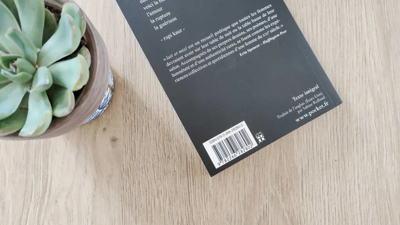 Un ean livre de poésie, "Lait et miel", est posé sur une table en bois, à côté d'une plante succulente.