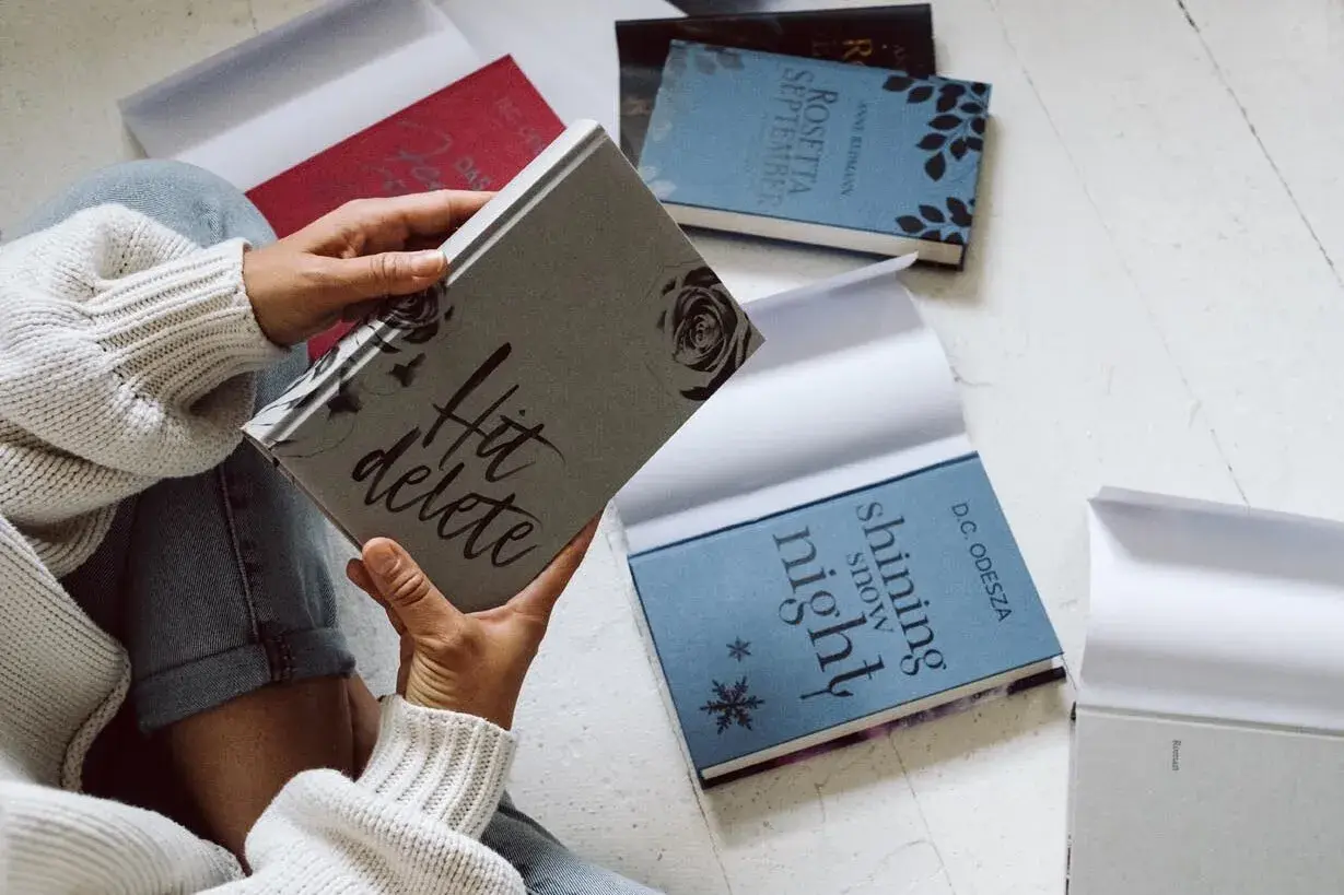 Une personne tient une jaquette de livre "Hit delete". D'autres livres sont disposés autour.