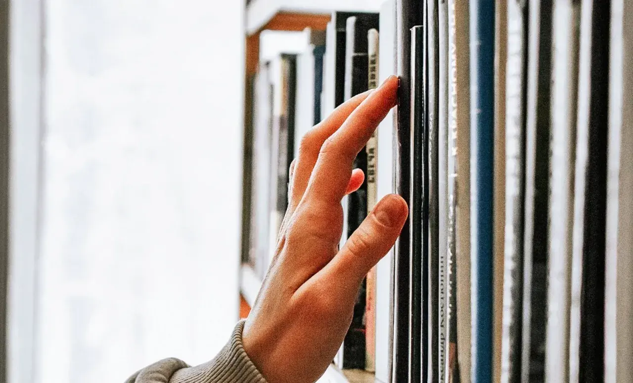 Main d'une personne effleurant une étagère remplie de livres, un voyage au cœur de la classique littérature.