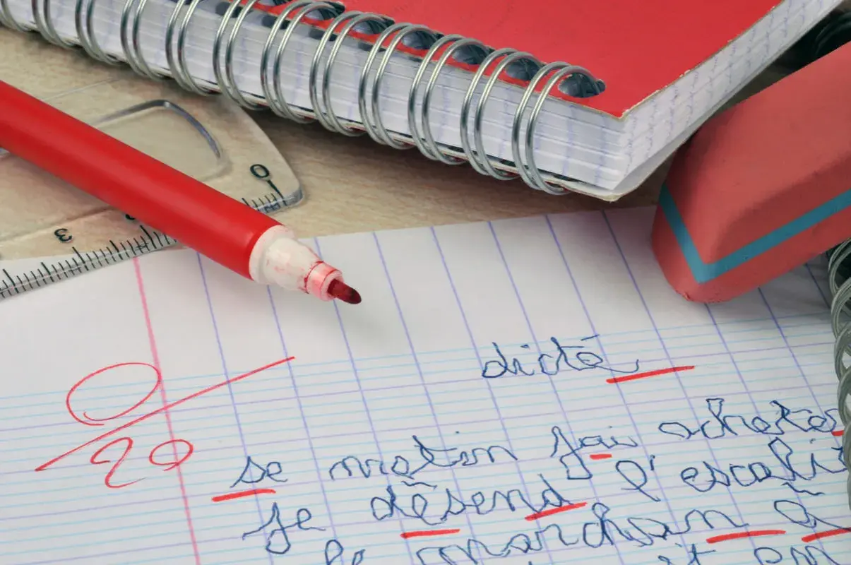 Un cahier, un stylo rouge et une gomme. La correction d'une dictée, une amplification de la figure de style "l'erreur", est en cours.