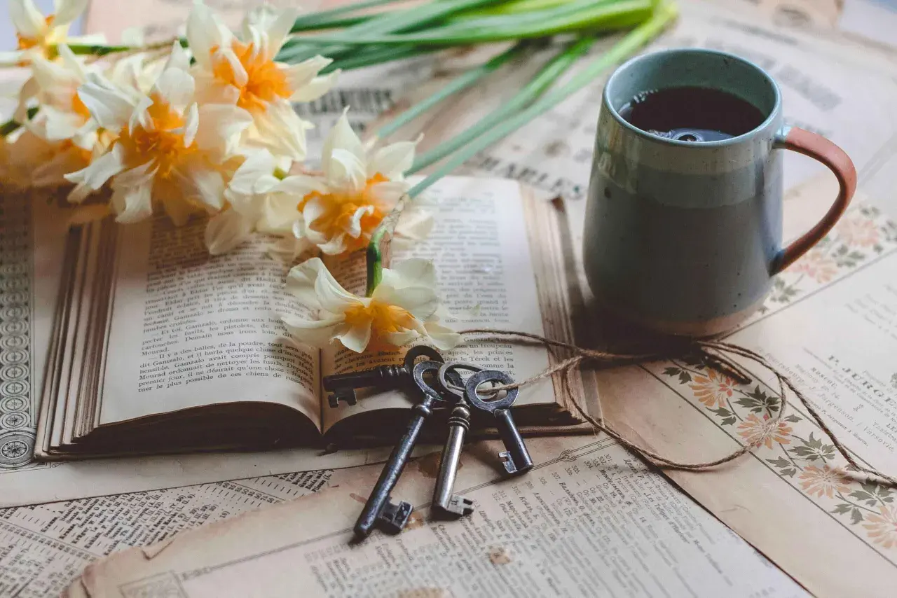 Un livre ouvert, des jonquilles, des clés anciennes et une tasse de thé. Le copyright livre est présent sur les pages jaunies.