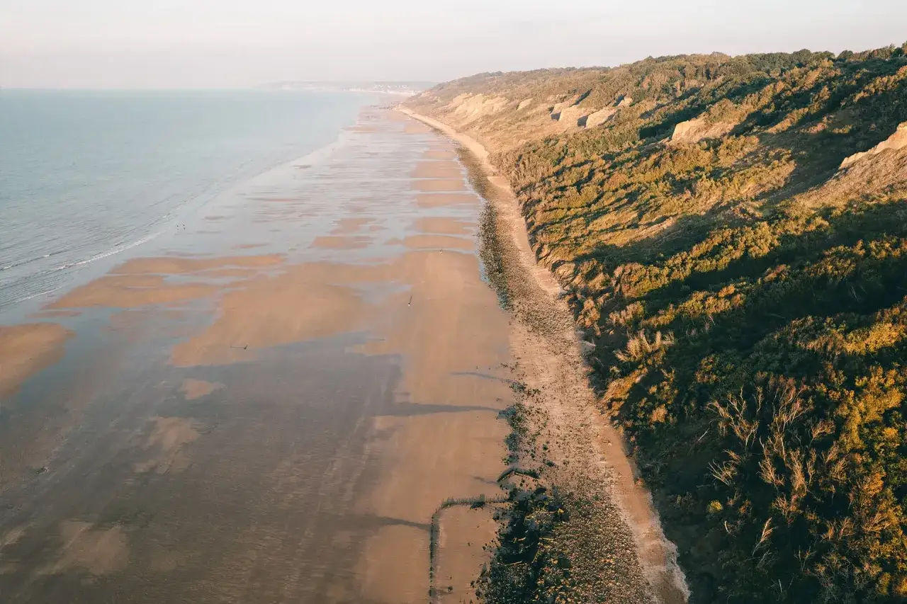 Plage immense, falaises verdoyantes. Un jour ce sera vide, explication fin. Le rivage s'étend à perte de vue, la nature règne.