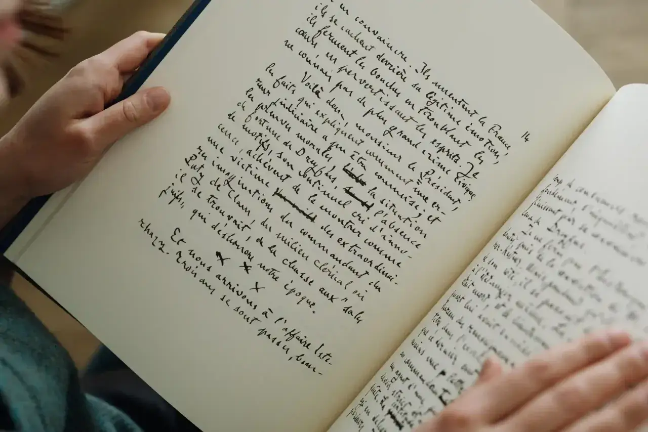 Mains tenant un livre ouvert, pages remplies d'une &eacute;criture manuscrite dense. Un aper&ccedil;u de la ligne &eacute;ditoriale des &eacute;ditions Grasset, peut-&ecirc;tre un manuscrit in&eacute;dit.